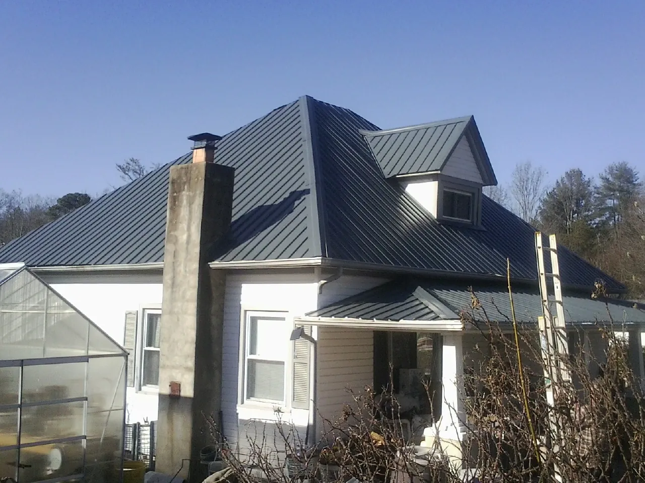 Dark blue standing seam metal roof on a white farmhouse with dormer — Slate & Tile Roof Repair by Roofing Brothers in Le Claire