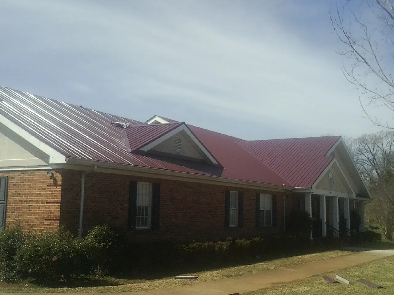 Red metal roof with gabled entries on a long brick building, from a Hail Damage Roof Repair job in Le Claire