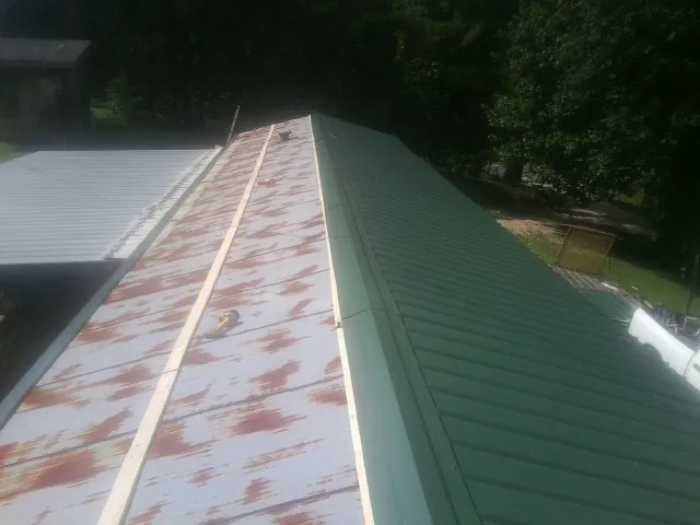 Old rusted panels beside newly installed green metal roofing — Wind Damage Roof Repair by Roofing Brothers in Le Claire