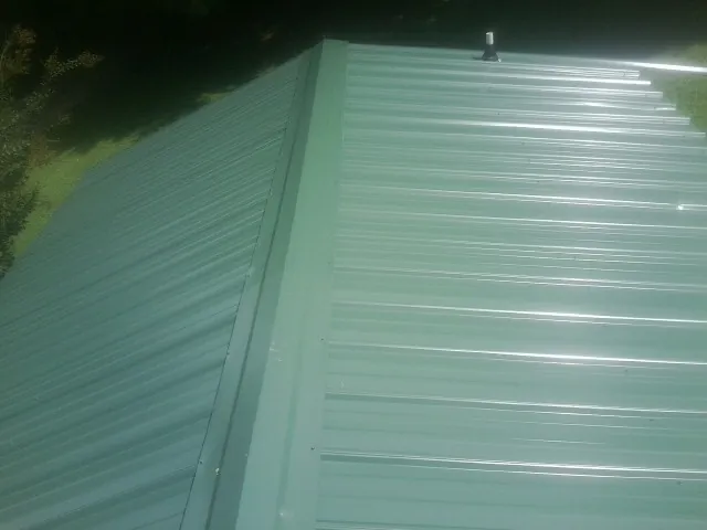 New green metal panels meeting at the ridge of a roof — Flat Roof Repair work by our crew in Le Claire