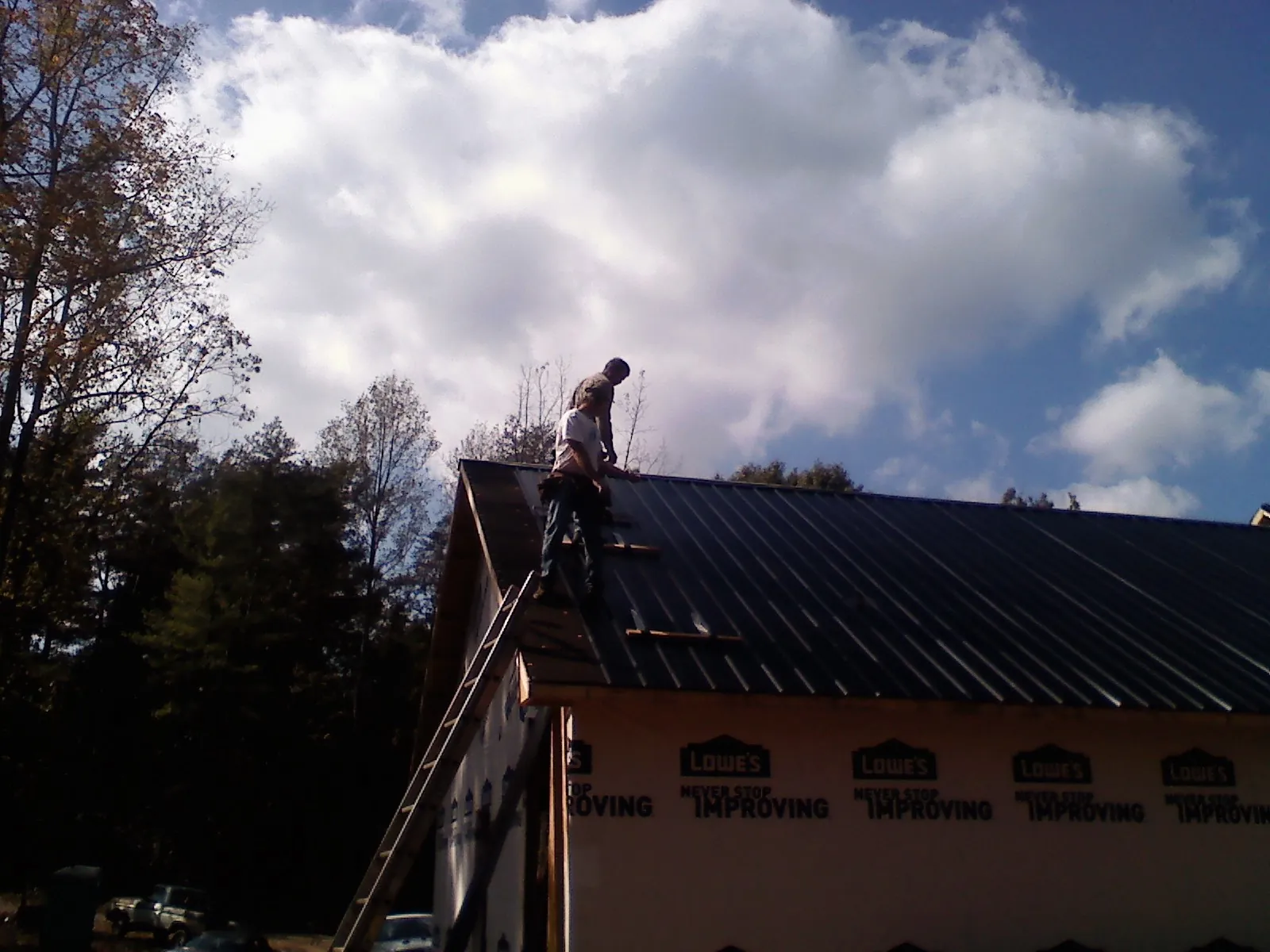 Roofer fastening dark metal panels high against a cloudy sky, from a Roof Inspection job in Le Claire