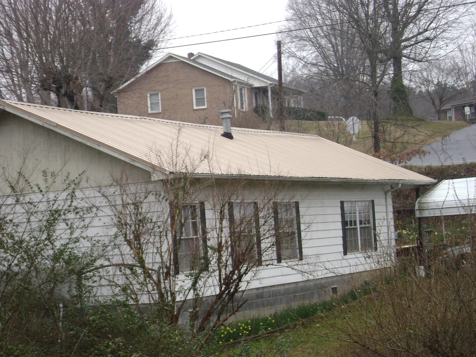 Tan metal roof on a white sided house set into a hillside — Commercial Roofing by Roofing Brothers in Le Claire