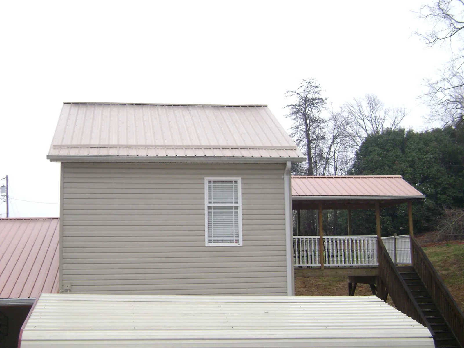 Tan metal roofs on a two story addition and attached porch, from a Roof Replacement job in Le Claire