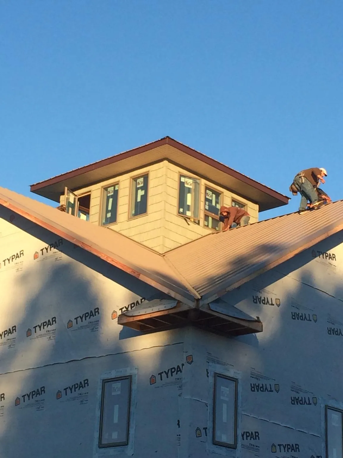 Roofers working around a rooftop cupola on a new metal roof at sunset — Roof Waterproofing in Le Claire by Roofing Brothers